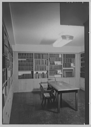 Black-and-white photograph of a 1951 record room with shelves of bound files, a central table and chairs