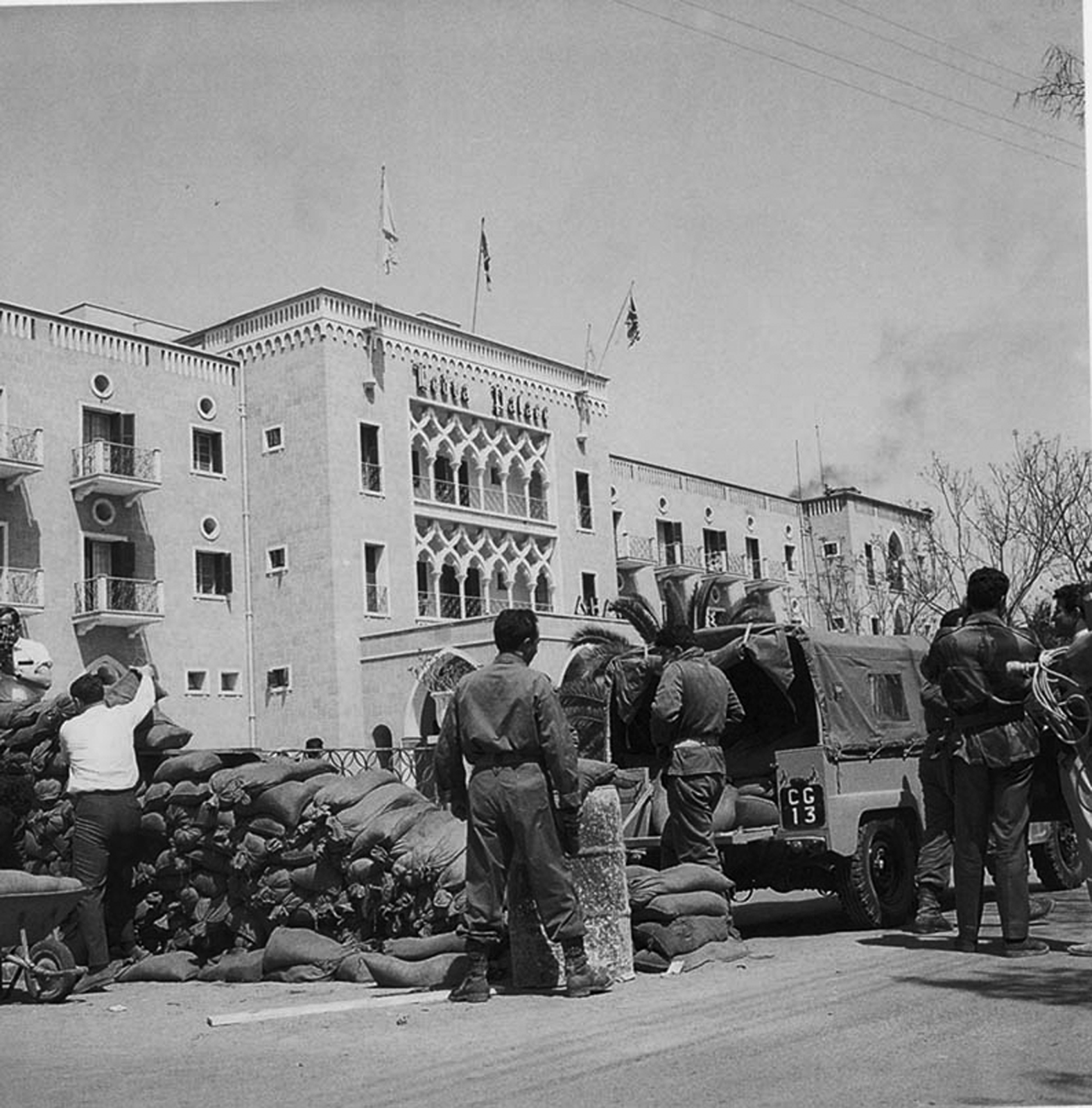 Historical black-and-white photograph of the first checkpoint outside the Ledra Palace Hotel in early 1964, with sandbags, armed men and a vehicle.